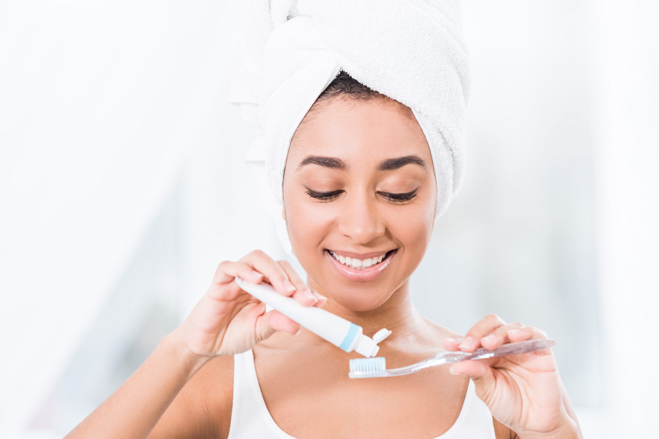 african american young woman with towel wrapped over head putting toothpaste on toothbrush