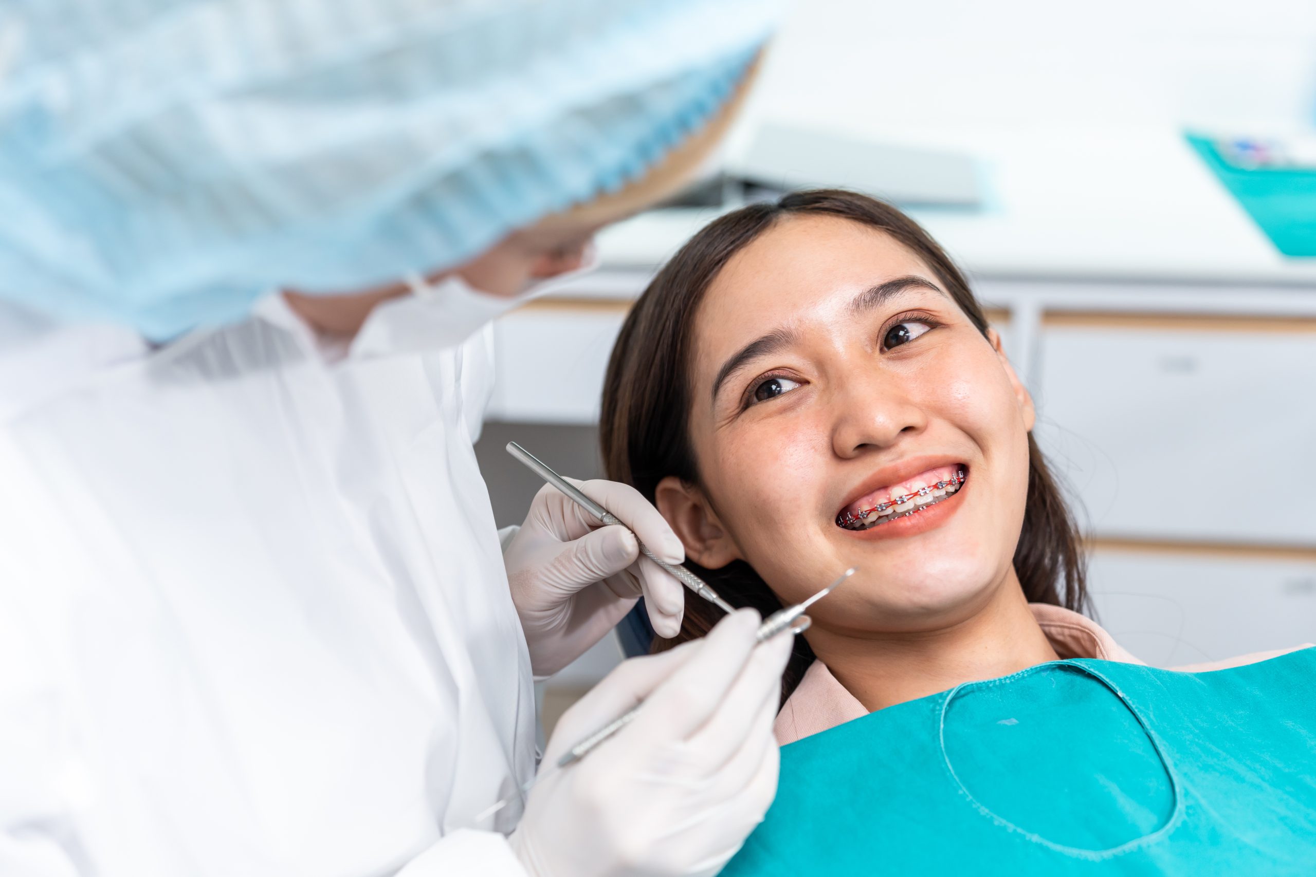 Orthodontist doctor examine tooth to woman patient at dental clinic. Attractive young girl with braces lying on dental chair, getting dental treatment from dentist during procedure service in hospital